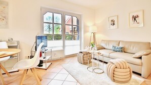 Een moderne woonkamer met een bank, een ronde salontafel en een televisie. Er is een raam met uitzicht op bomen en een gebouw.