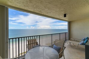 Un balcón con una mesa y sillas de vidrio, con vista a una playa y el océano.