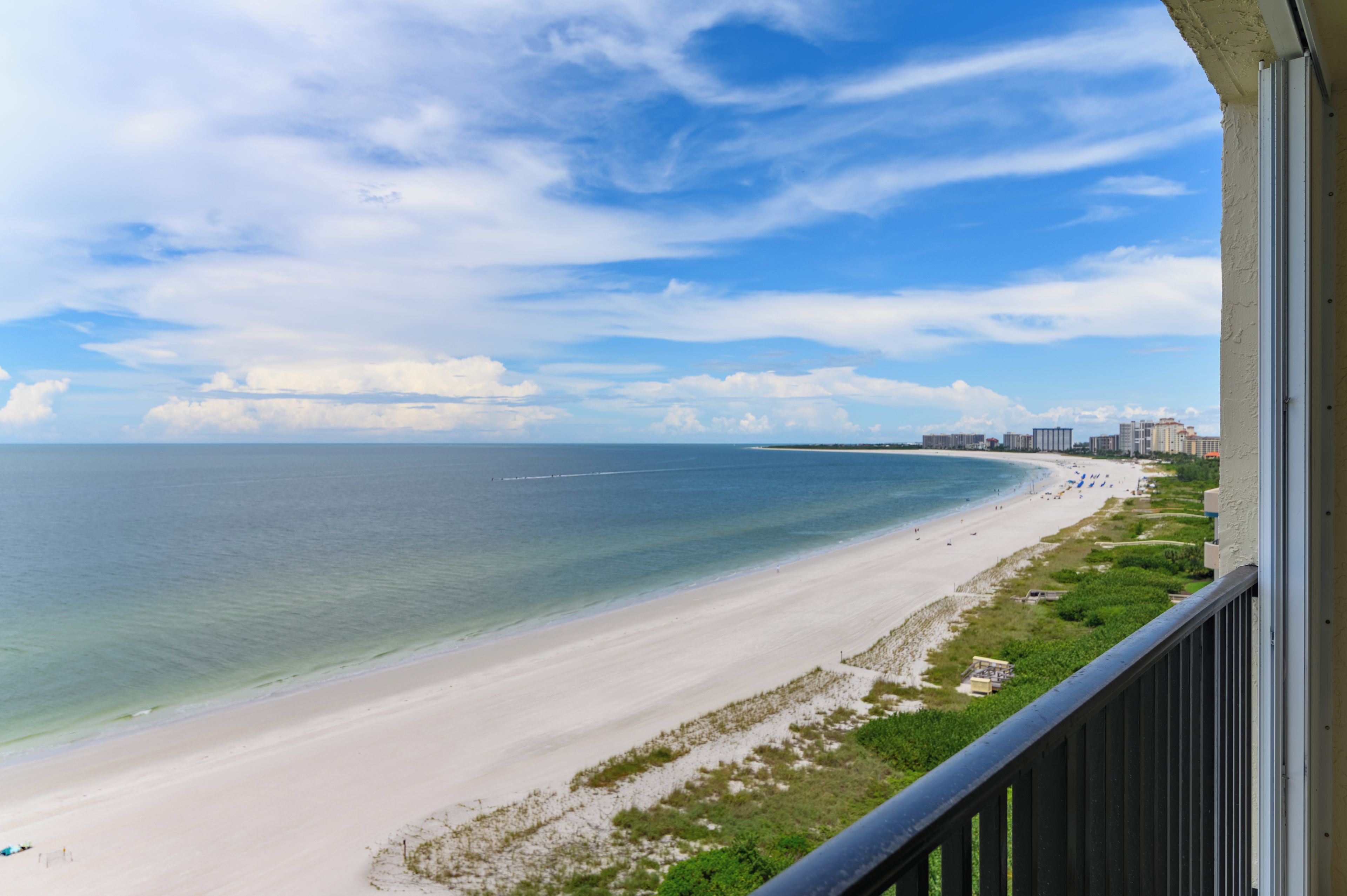 A beach view from a balcony with a clear sky and calm sea.