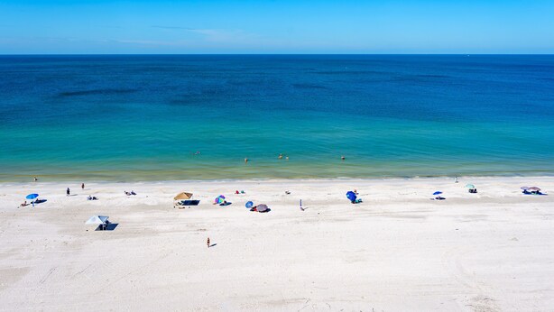 Ein Strand mit klarem, blauem Wasser, weißem Sand und mehreren Sonnenschirmen.