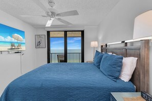 Een slaapkamer met een groot bed, een plafondventilator, uitzicht op het strand en een schilderij van een vogel.