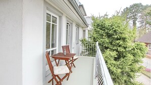 Een balkon met een houten tafel en stoelen, een witte balustrade en een grote altijdgroene boom.