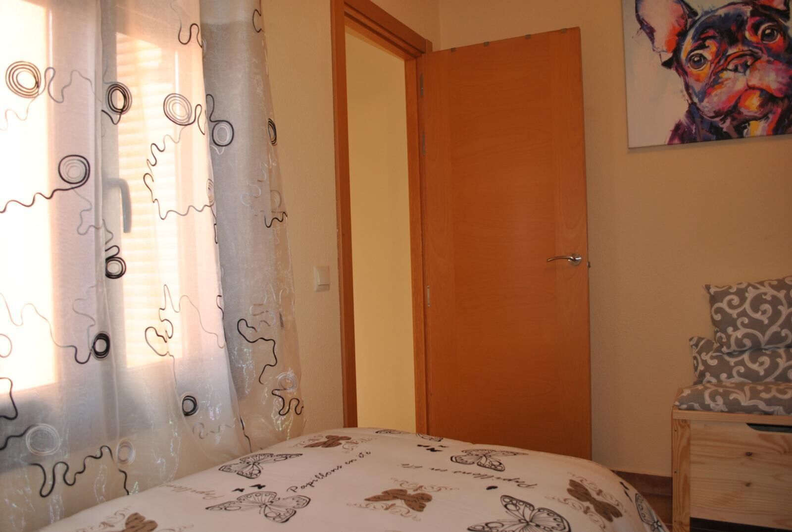 Un dormitorio con una cama, una puerta de madera, una mesita de noche y un cuadro en la pared.