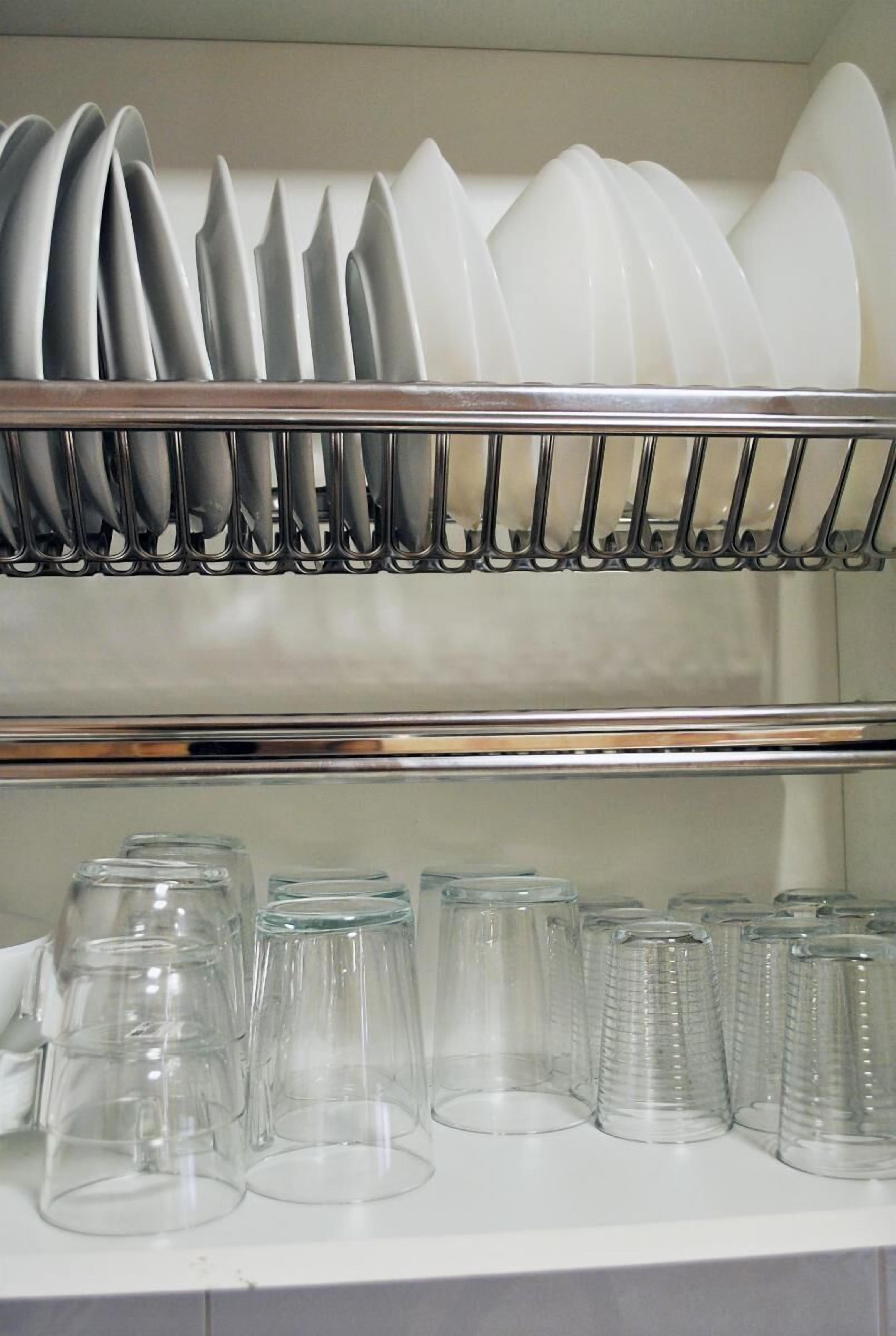 A kitchen with a dish rack holding white plates and a row of clear glass cups below.