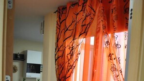 A hallway with orange curtains, a tiled floor, and a kitchen area in the background.