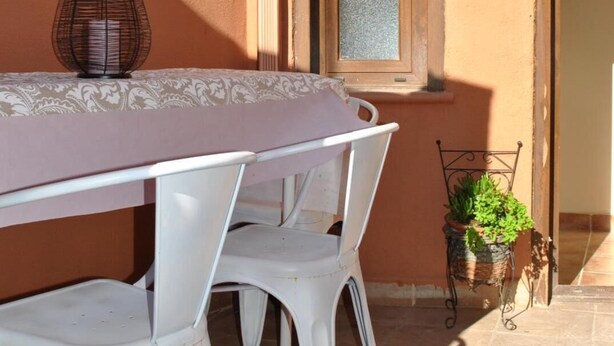 A table with a white tablecloth and two white chairs, a lantern, and a potted plant on a tiled patio.
