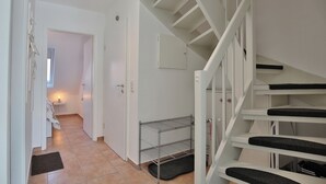 En stilren, modern hall med en trappa som leder upp till andra våningen. En hylla i metall står längs väggen, och en dörr syns i bakgrunden.