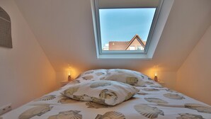 Ett sovrum med ett takfönster, en säng med ett blommigt överkast och två sänglampor.
