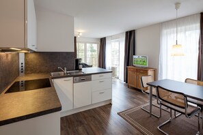 Een moderne keuken met een inbouwfornuis, witte kasten en een eethoek met een tafel en stoelen.
