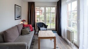 Una sala de estar con un sofá, una mesa de centro, una silla y vistas a un jardín a través de un ventanal.