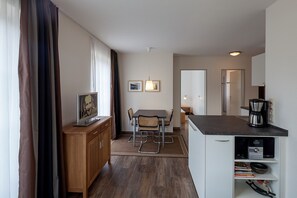 A compact kitchen with a dining table, chairs, a coffee maker, and a small cabinet.