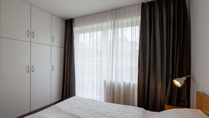 Un dormitorio con cama, armario, ventana con cortinas y lámpara de noche.