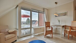 A modern living room with a sofa, two wicker chairs, a dining table, and a large window with a view of the outside.