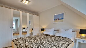 A bedroom with a bed, white nightstands, a mirror, and a painting on the wall.