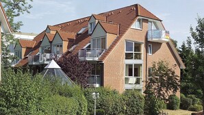 A multi-story residential building with a brick facade, multiple windows, and a sloped roof.