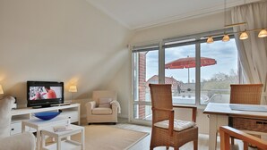 A modern living room with a television, white furniture, a large window with a view of the outside, and a red umbrella outside.