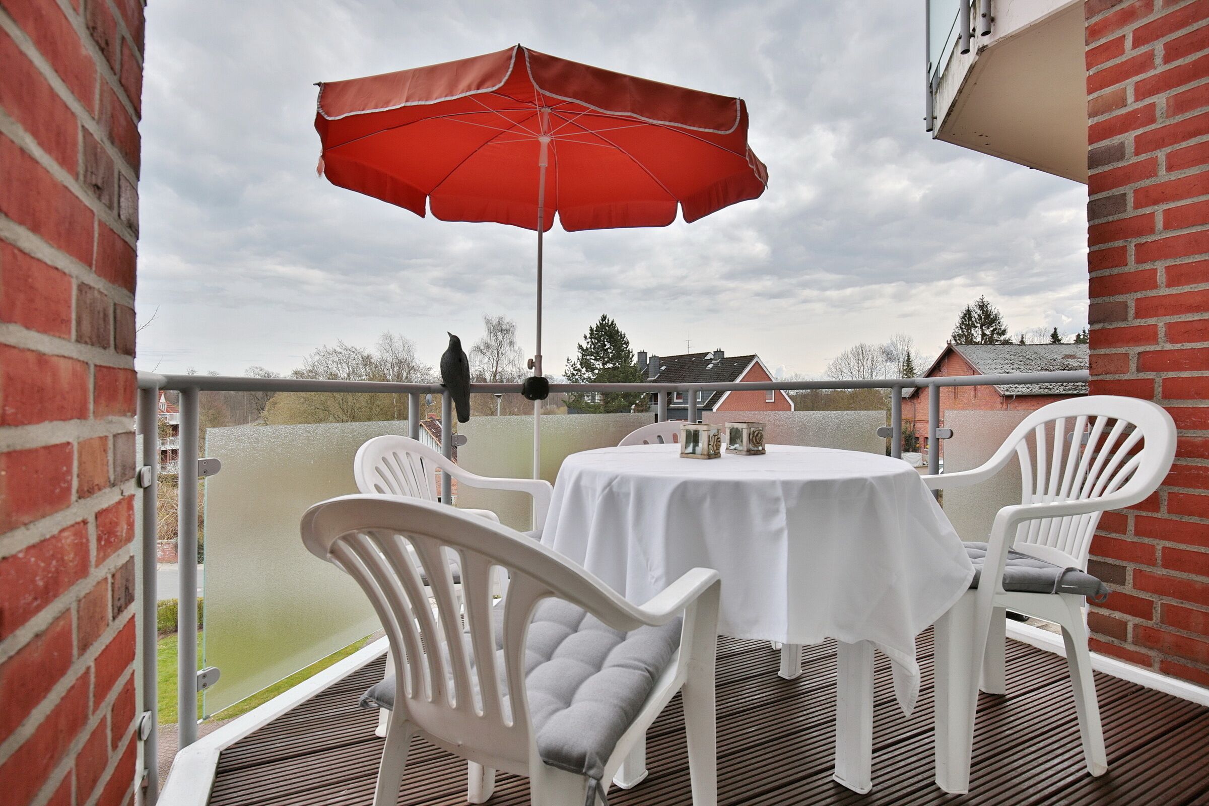 An outdoor patio with a table and chairs, a red umbrella, and a view of the surrounding area.