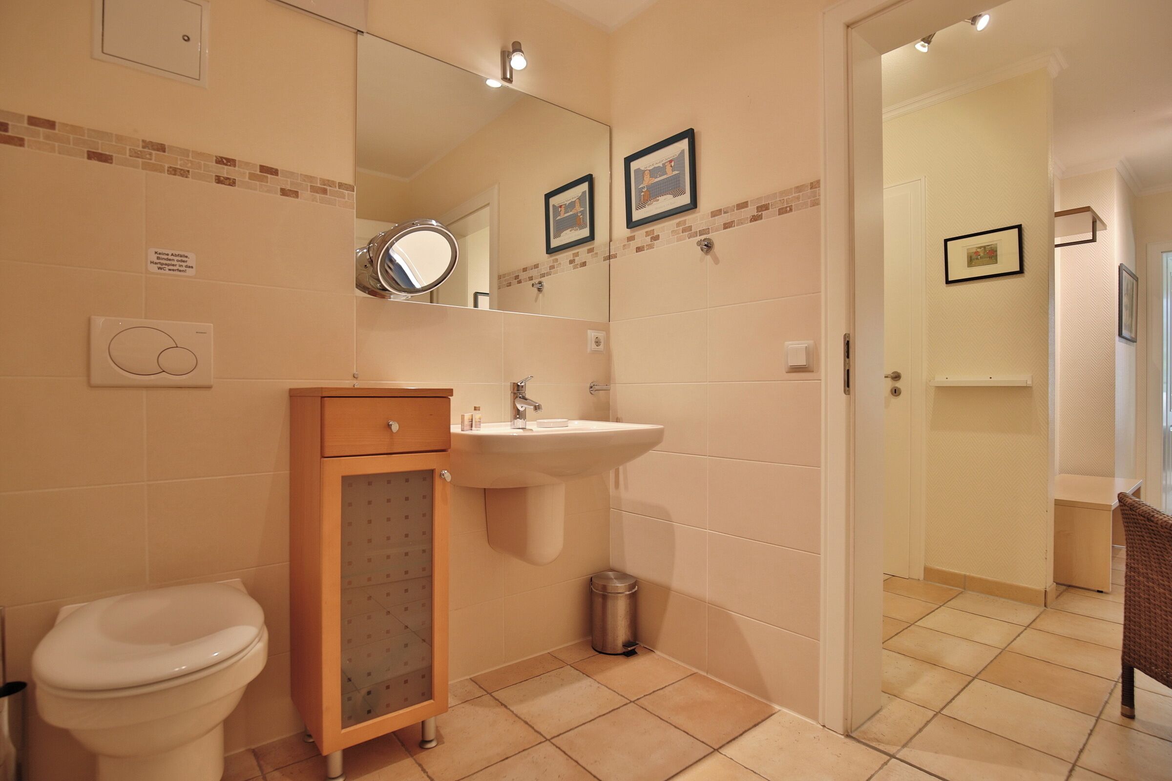 A bathroom with a toilet, sink, and mirror. There is a trash can and a cabinet.