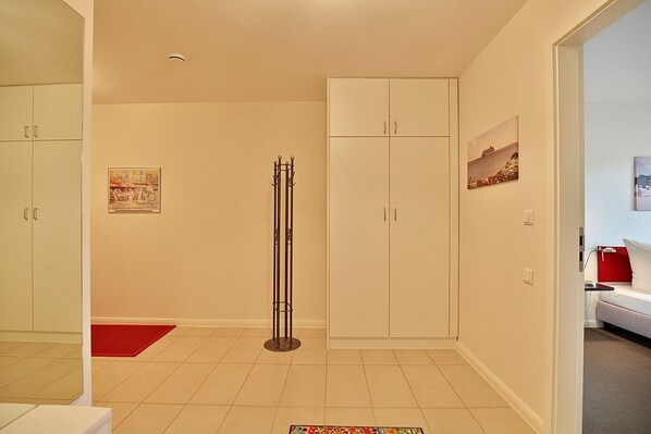 Une pièce avec un placard, un porte-manteau, un tapis rouge et un tableau accroché au mur.