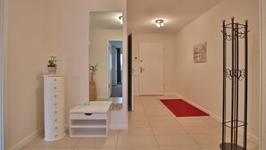 A hallway with a white dresser, a small table, a red rug, and a coat rack. - Villa Mér Baltique Appartement 13 (Timmendorfer Strand)