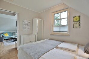 A bedroom with a bed, a wardrobe, a window with blinds, a sofa, and a coffee table in the adjacent living area. - Am Rosenhain 6 Appartement 5 (Timmendorfer Strand)
