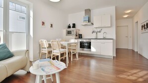 Una cucina moderna con mobili bianchi, forno integrato e macchina per il caffè. È presente un'area pranzo con tavolo e sedie.