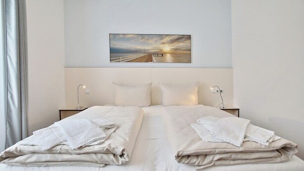 Una camera d'albergo con un letto grande, due comodini, un'opera d'arte appesa al muro e vista sul mare al tramonto.