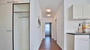 Un pasillo con suelo de madera, paredes blancas y una zona de cocina con armarios y un lavabo.