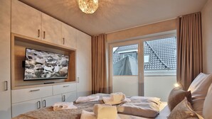 Ett hotellrum med en stor, platt-TV som är monterad på väggen, en säng med prydligt vikta handdukar och ett fönster med gardiner.