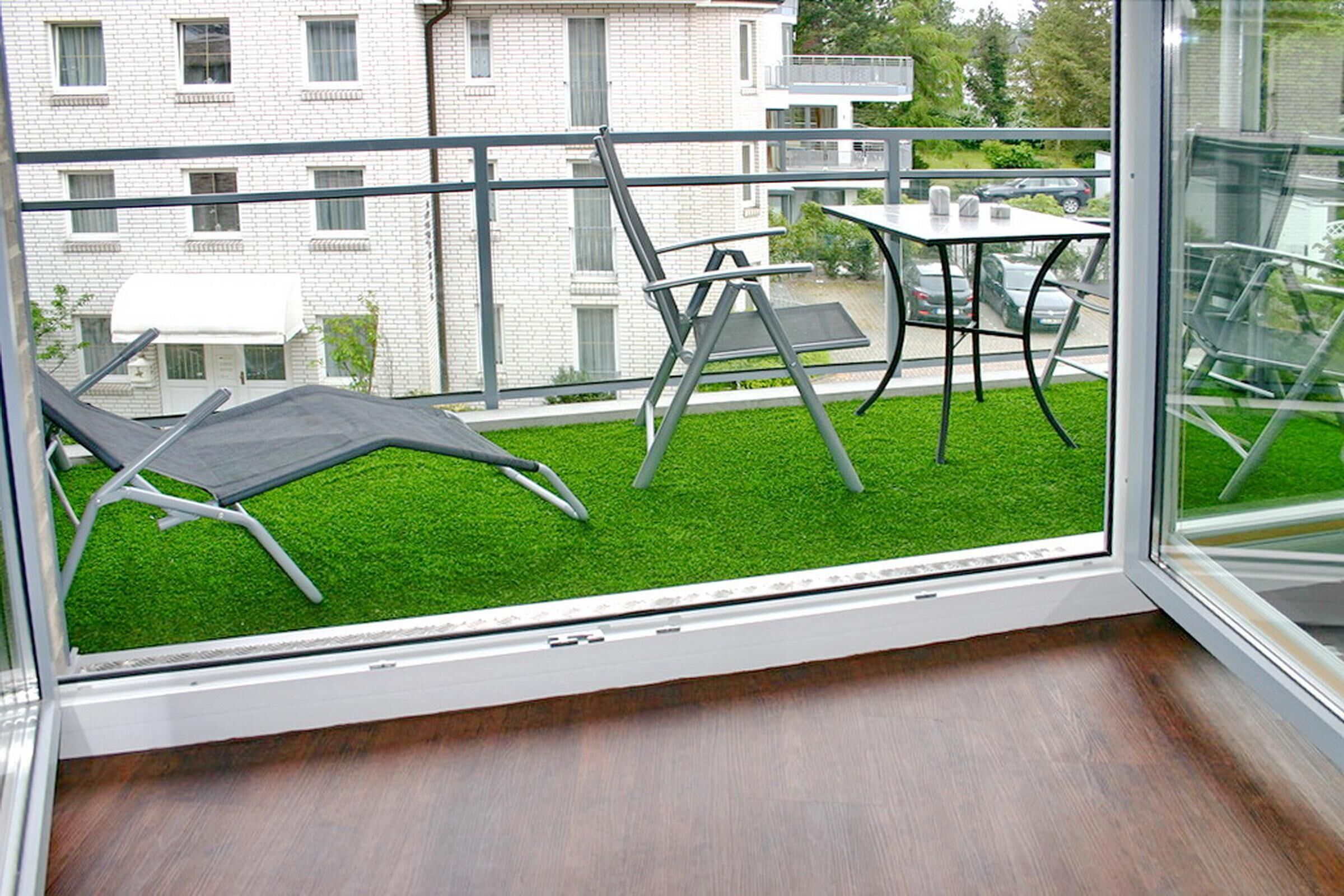 Un balcón con vista a un área verde, una mesa y dos sillones de relax.