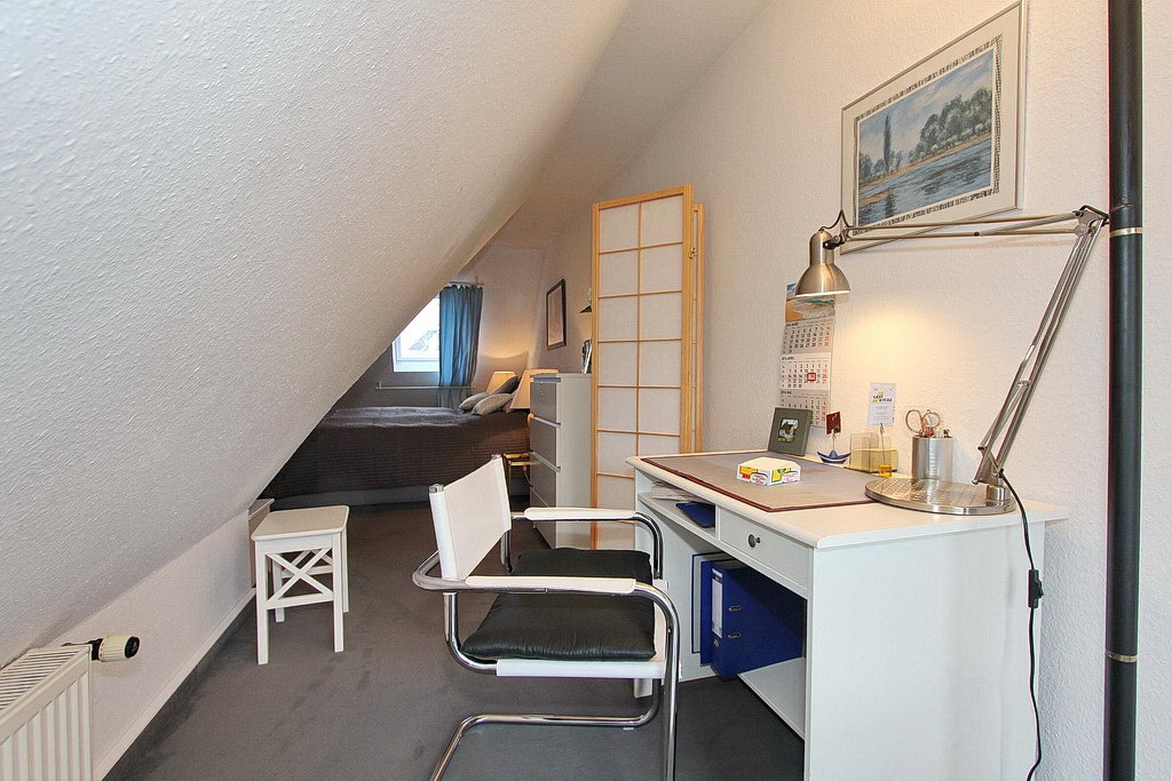 A small, compact room with a desk, chair, and a bed. There is a window with a view of trees and a building.