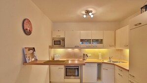 A compact kitchen with a microwave, oven, and sink. There is a small countertop and a cabinet above the sink. - Villa Mér Baltique Appartement 20 (Timmendorfer Strand)