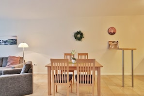 A dining area with a wooden table and chairs, a small potted plant, and a wall-mounted clock. - Villa Mér Baltique Appartement 20 (Timmendorfer Strand)
