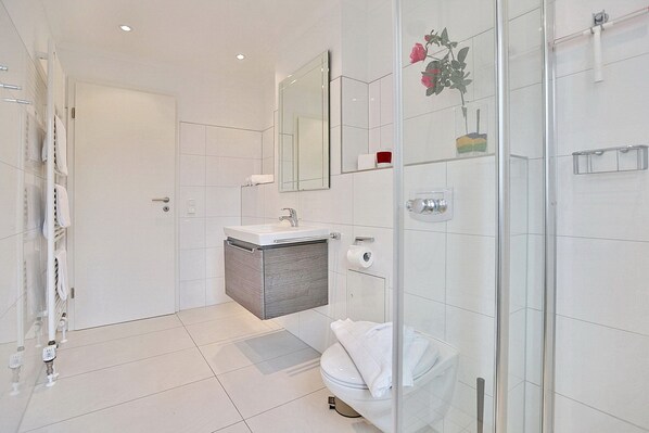 A modern bathroom with a glass shower enclosure, a white toilet, and a vanity with a mirror. - Seaside Residence, Apartment 7 (Timmendorfer Strand)