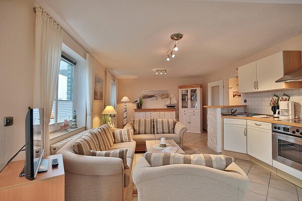 Un espace de vie compact comprenant un canapé, des fauteuils, une petite table, un téléviseur et une kitchenette équipée d’une cuisinière et d’un four.