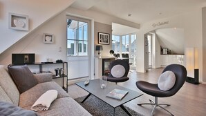 Ein modernes Wohnzimmer mit Sofa, Couchtisch und Sessel. Im Hintergrund ist eine Küche zu sehen.