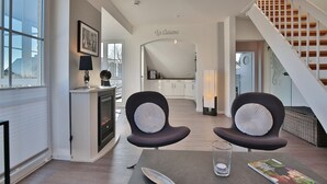 Ein modernes Wohnzimmer mit Kamin, einem Esstisch mit Stühlen, einer Treppe und einer Küche im Hintergrund.