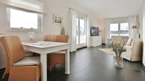 Ett modernt vardagsrum med en matplats, stora fönster och en platt-TV.