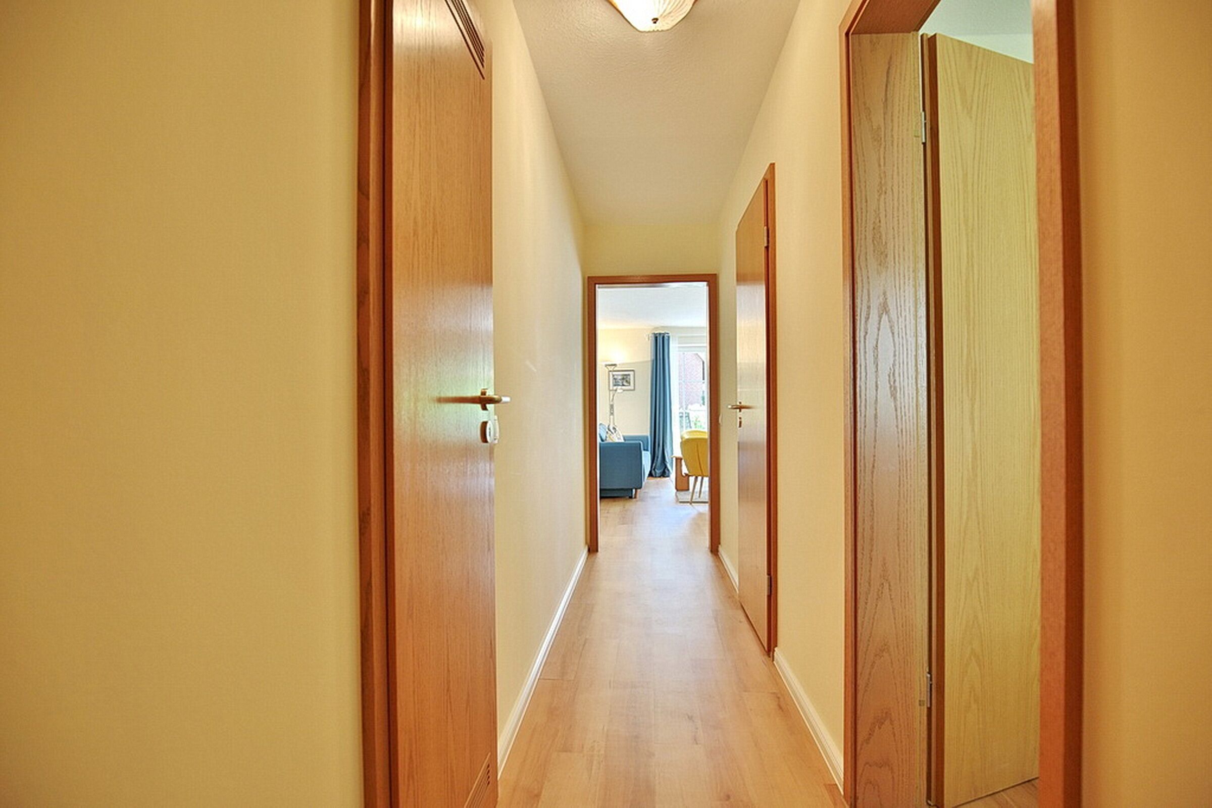 A hallway with wooden doors and a light-colored floor, leading to a room with a blue curtain.