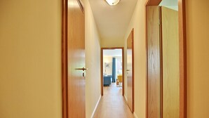 A hallway with wooden doors and a light-colored floor, leading to a room with a blue curtain. - Gorch-Fock-Park 57 Apartment 17 Beach pleasure (Timmendorfer Strand)