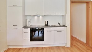 A compact kitchen with white cabinets, a built-in oven, a coffee maker, and a sink. - Gorch-Fock-Park 57 Apartment 17 Beach pleasure (Timmendorfer Strand)