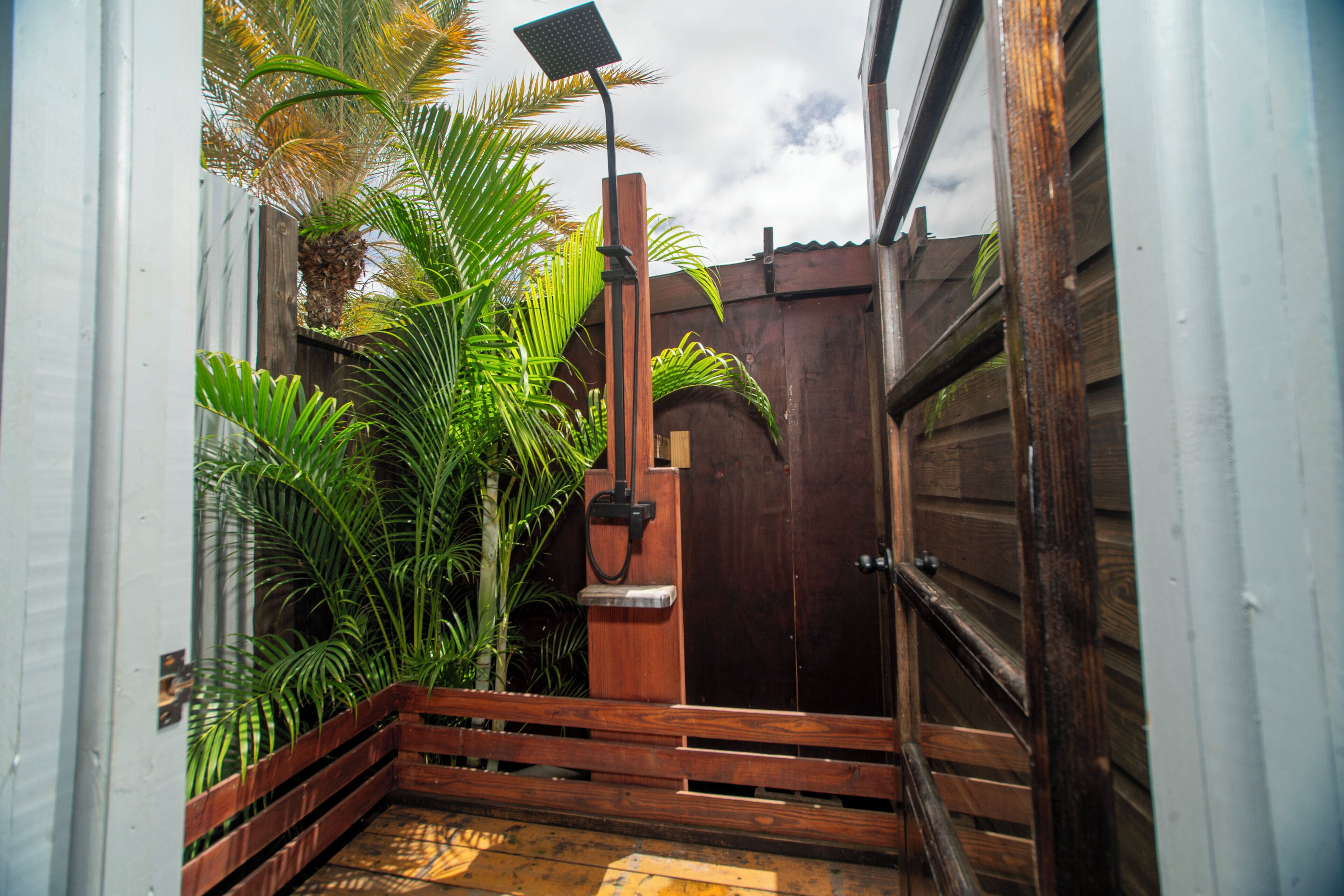 A wooden gate leading to a patio area with a wooden bench and a solar-powered outdoor shower.