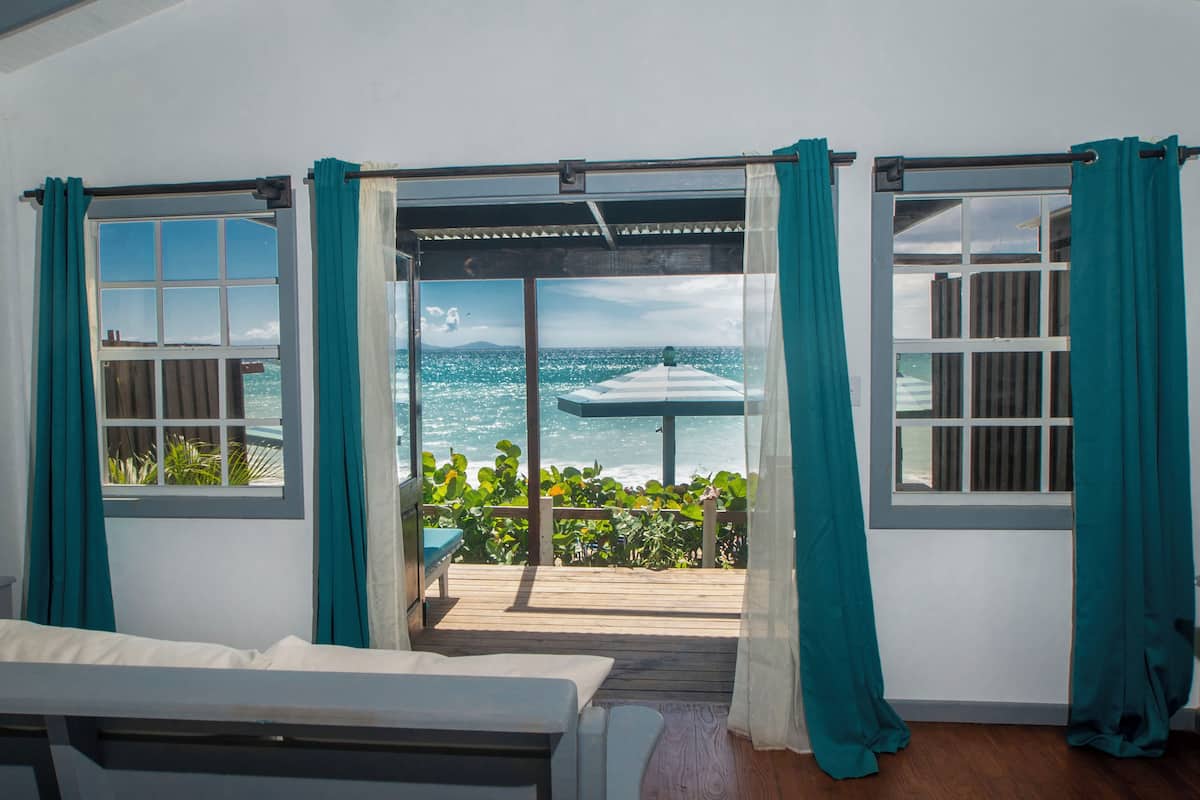 A room with a view of the ocean, a wooden deck, and a bench.