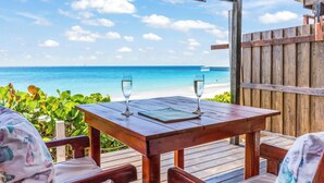 A wooden deck with a table and chairs, overlooking a beach with clear blue water and a wooden fence. - Conch Beach Cabins - Rumbus Beach (Johnson's Point)