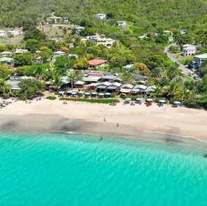 An aerial view of a coastal resort with multiple buildings, a sandy beach, and clear turquoise waters.