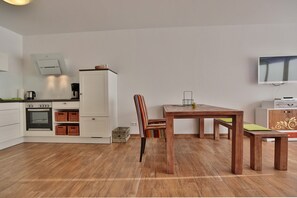 Une cuisine moderne avec des meubles blancs, une table à manger en bois et un téléviseur fixé au mur.