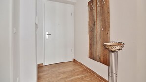 A hallway with a white door, a wooden wall with metal hooks, and a floor lamp. - Die Wolburg Appartement 6 (Timmendorfer Strand)