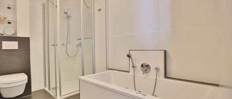 Un baño moderno con ducha envuelta en vidrio, inodoro blanco y bañera independiente.