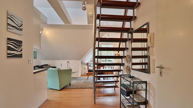 Ein geräumiger Flur mit Holzboden, einer Treppe mit Glastrennwand und einem Küchenbereich im Hintergrund.