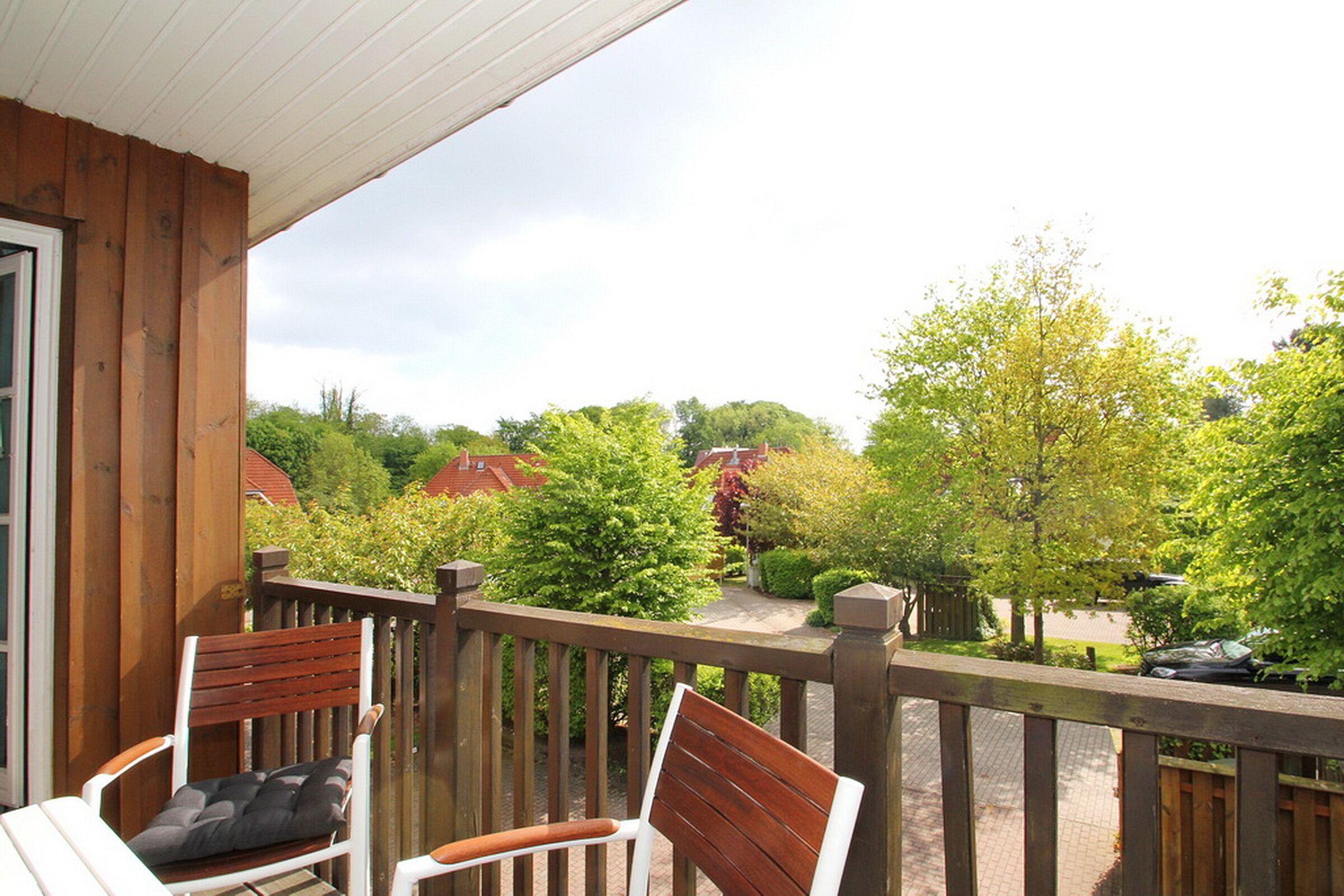 A wooden deck with two chairs and a view of a residential area with trees and houses.